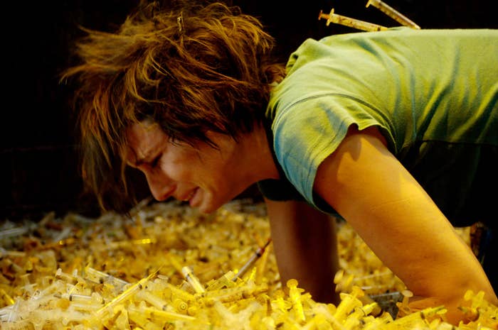 A woman is crying as she is elbows deep inside a mountain of dirty syringes.