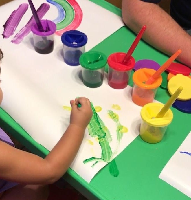 Reviewer&#x27;s child painting with the colorful paint cups sitting on the table
