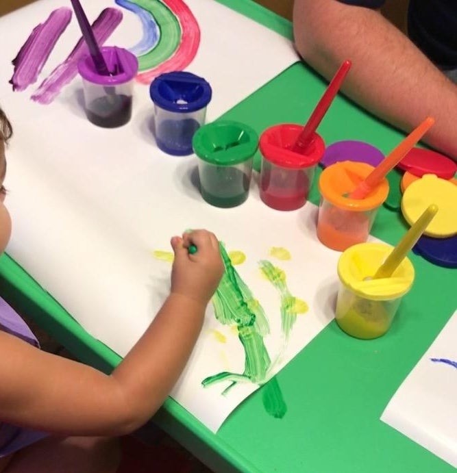 Reviewer&#x27;s child painting with the colorful paint cups sitting on the table