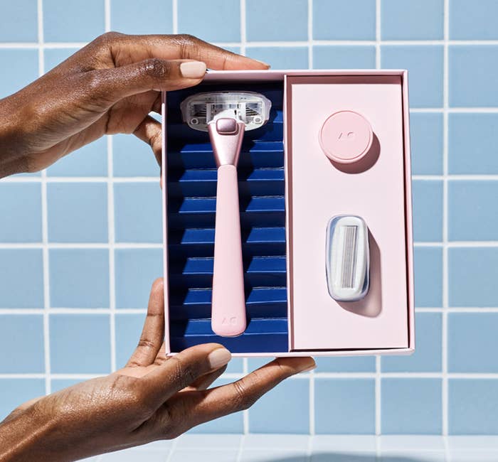 the razor kit with pink razor, refillable blade, and magnetic hook in model&#x27;s hands