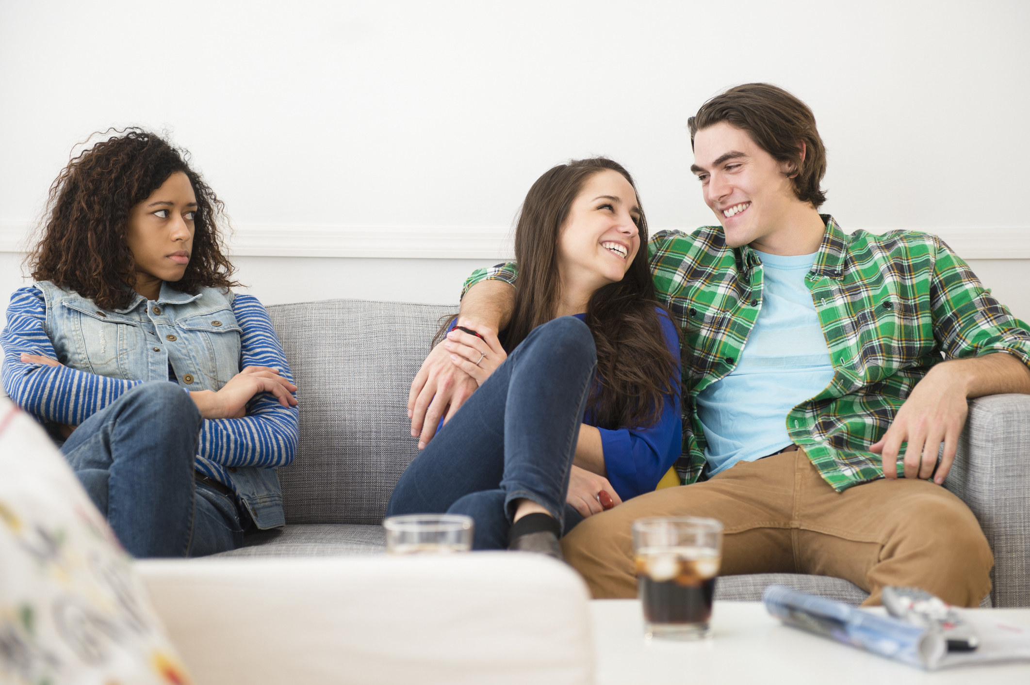 a couple sitting cozily together on a couch, next to a woman who looks left out