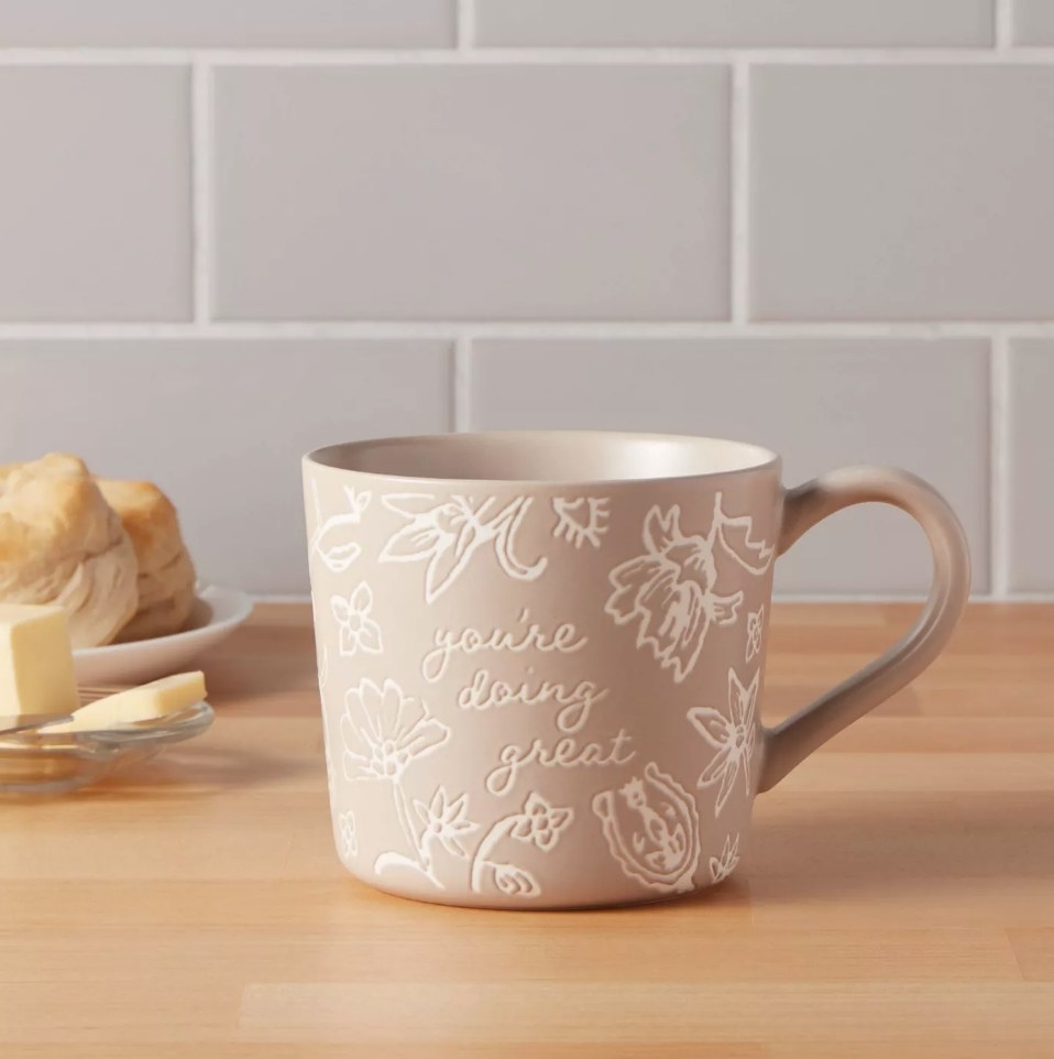Tan mug with floral engravings and &quot;you&#x27;re doing great&quot; engraved in the center