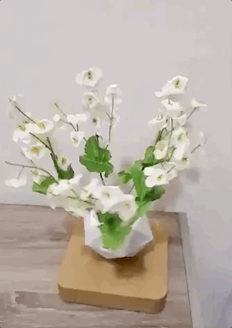 a gif of a planter filled with white blossoms levitating over a light-colored wood base