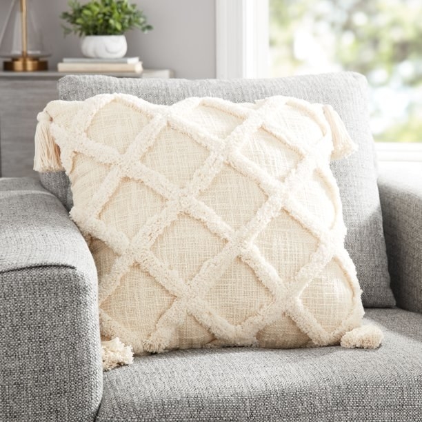 Cream colored tufted pillow with diamond pattern and tassels