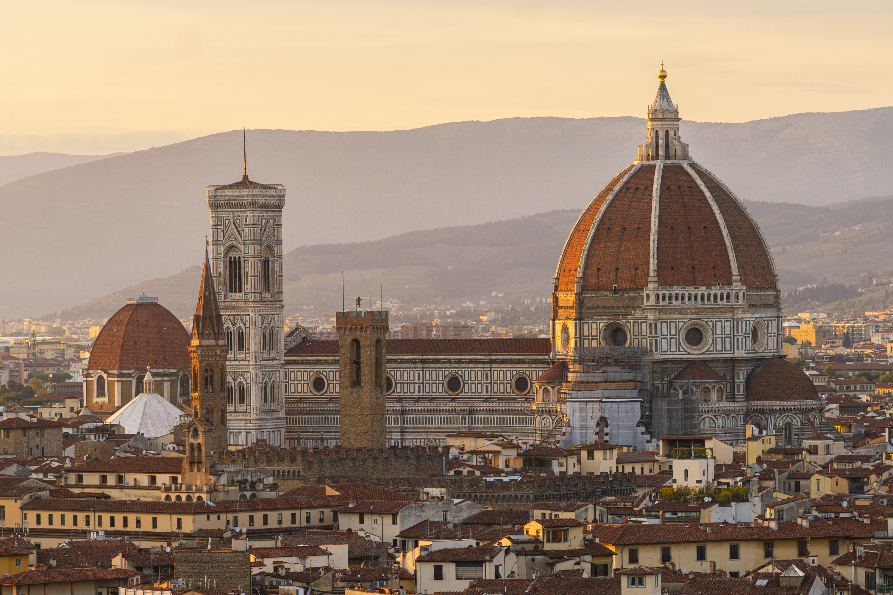 The Florence skyline during golden hour with a hazy mountain range behind the duomo