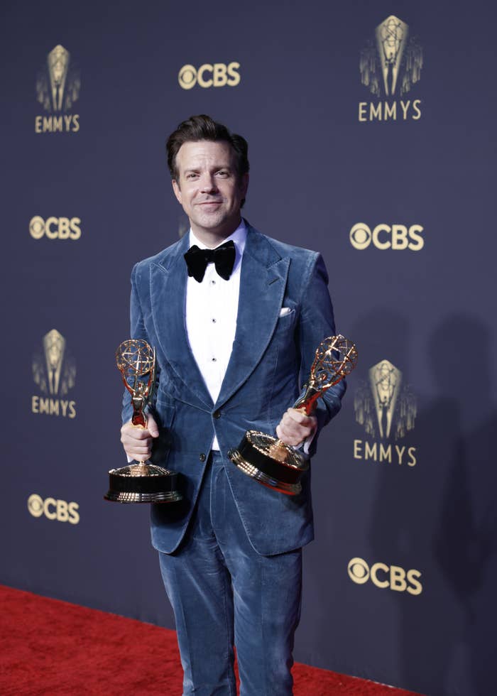 Sudeikis holds two Emmys while wearing a tuxedo on the red carpet