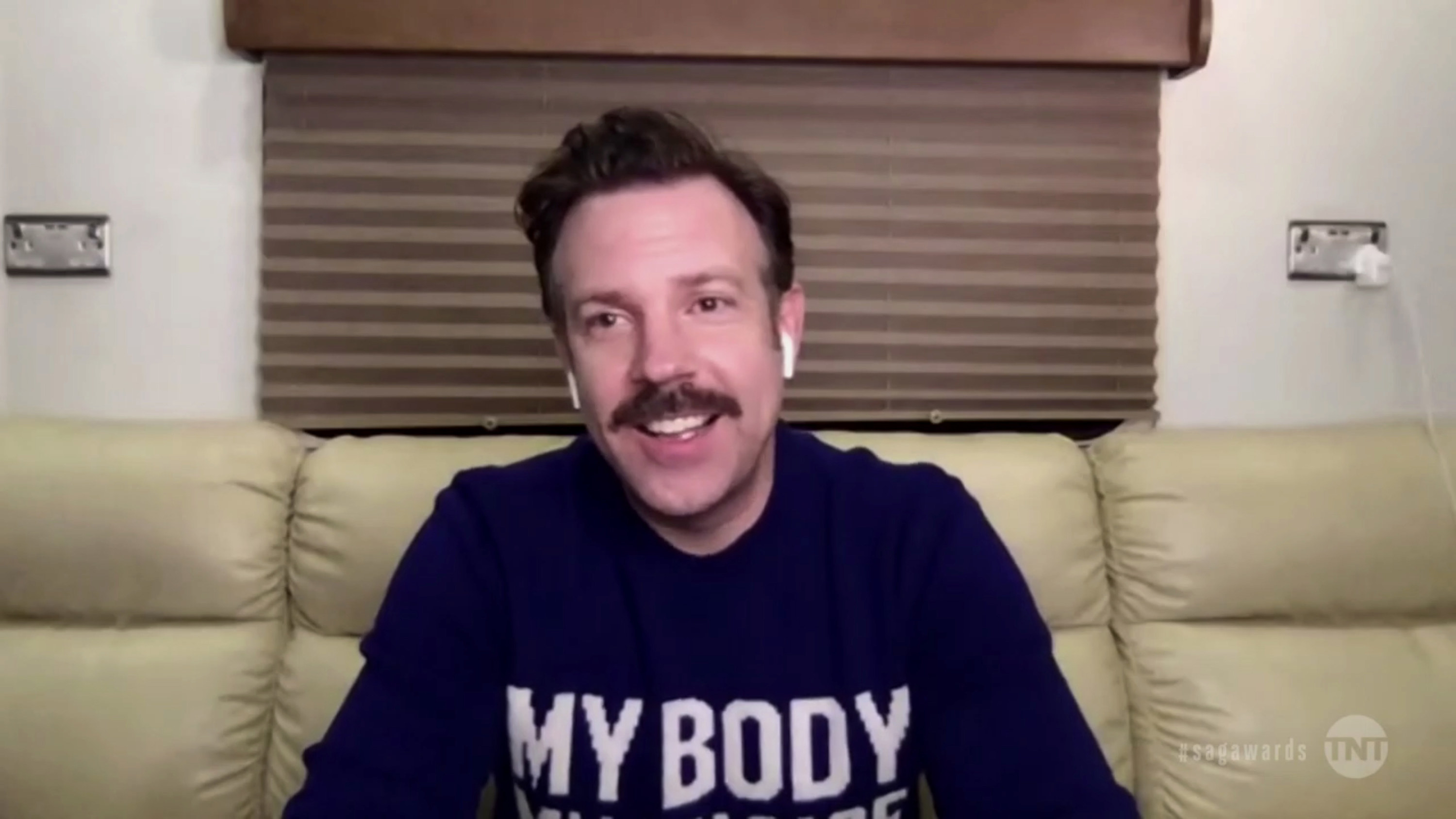 Sudeikis wears a &quot;My Body My Choice&quot; shirt and AirPods while sitting on a sofa
