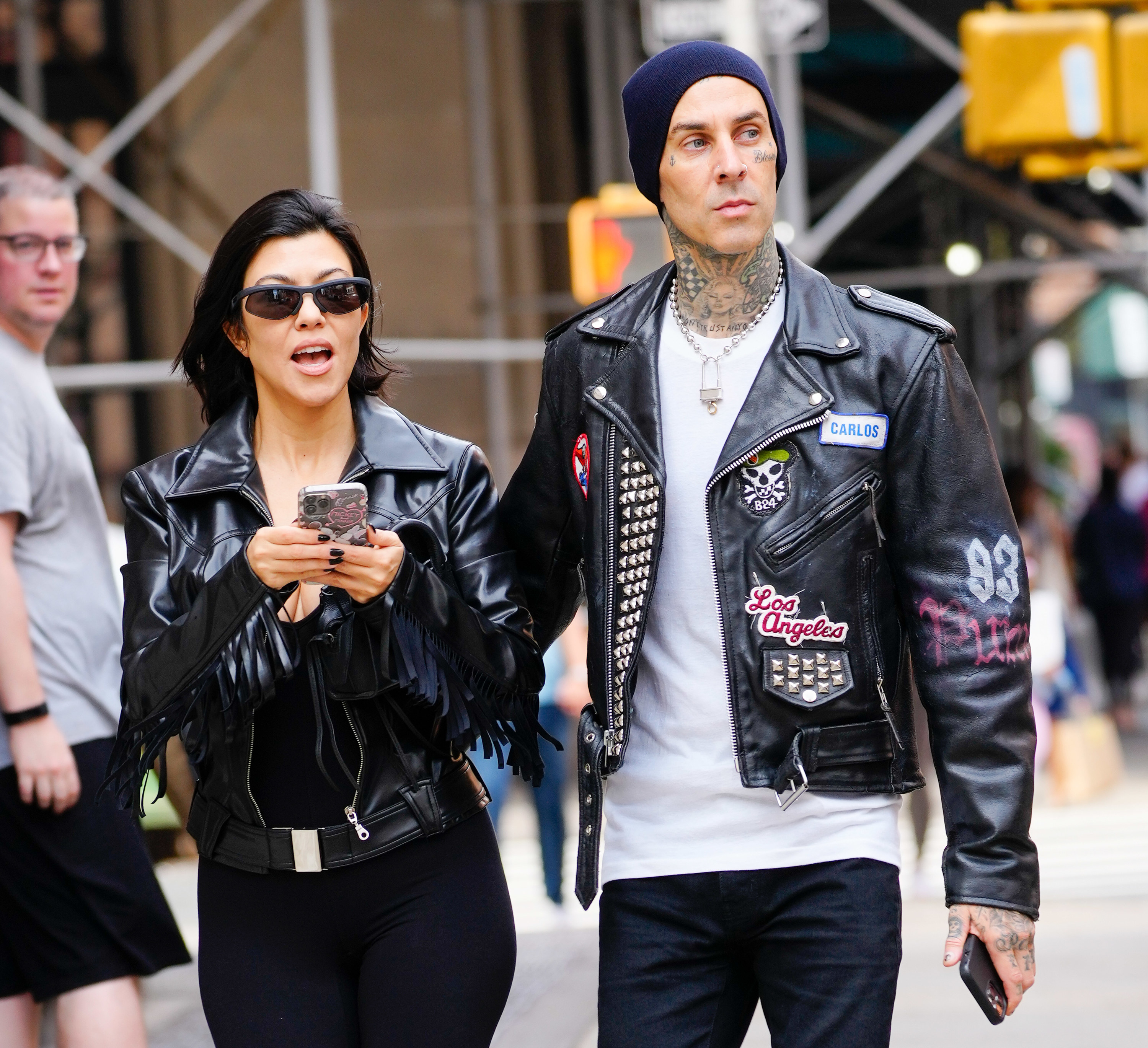 Kourtney holds her phone while walking down the street as Travis puts his hand on her back