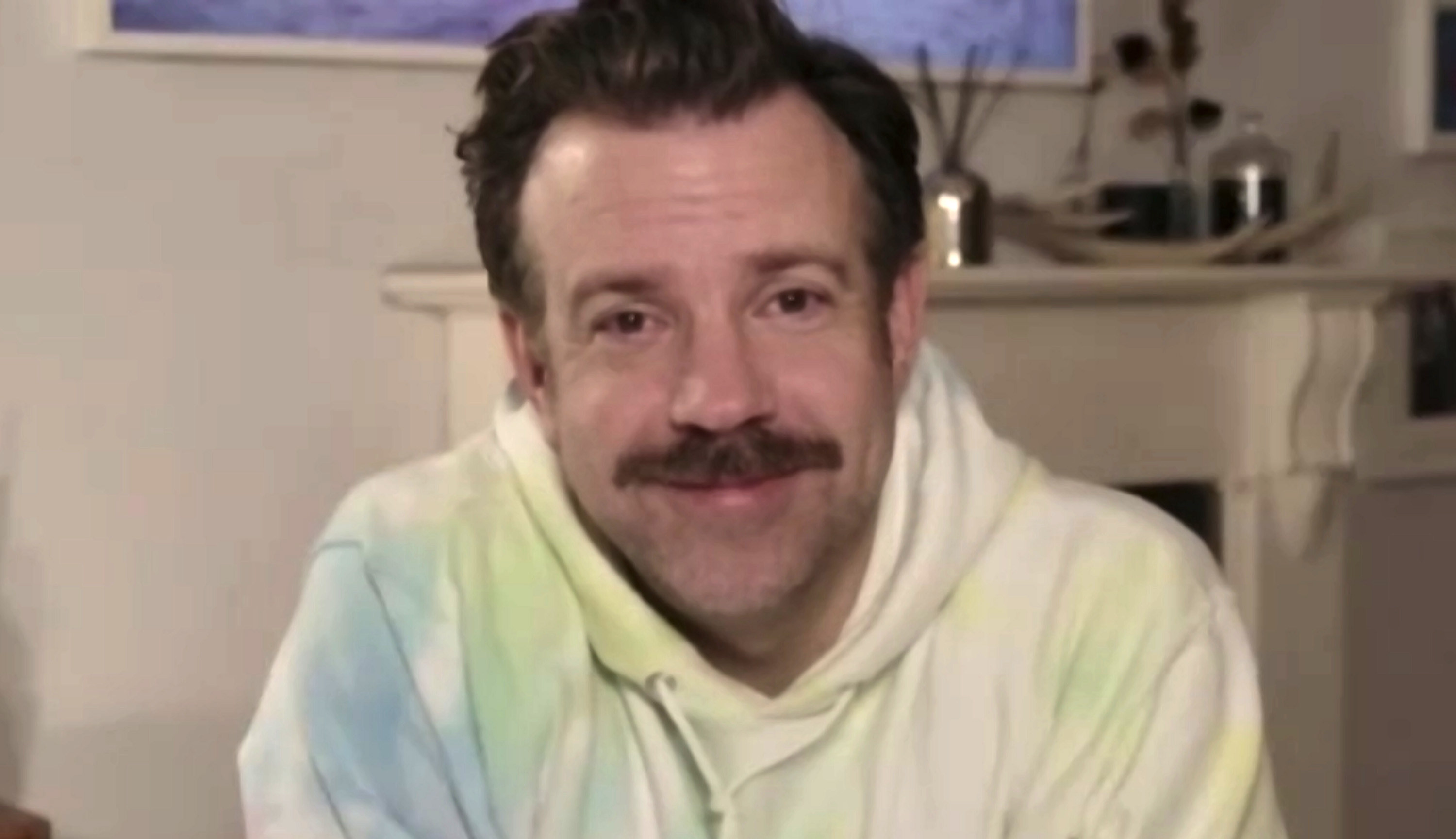 Sudeikis smiles into the camera while wearing a tye-dye sweatshirt