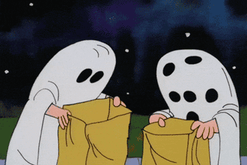 Charlie Brown as a ghost, with too many eye holes, holds up a rock.