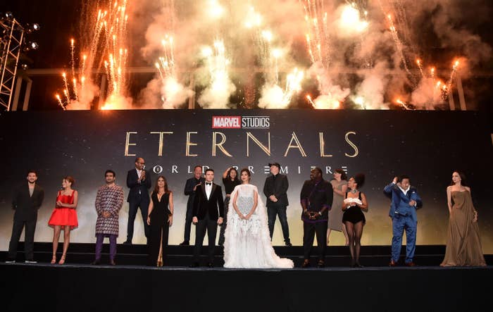 Cast members in front of an Eternals world premiere banner and fireworks