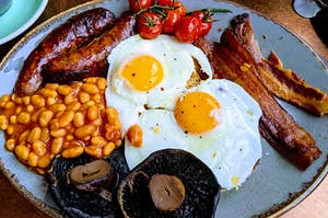 An English breakfast spread is shown with eggs, beans, bacon, sausage, mushrooms and tomatoes