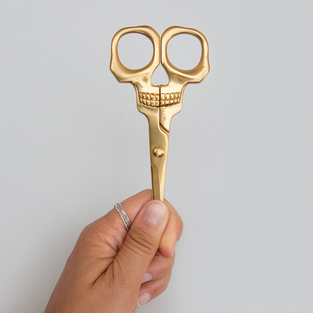 a person holding up a pair of brass scissors shaped like a skull