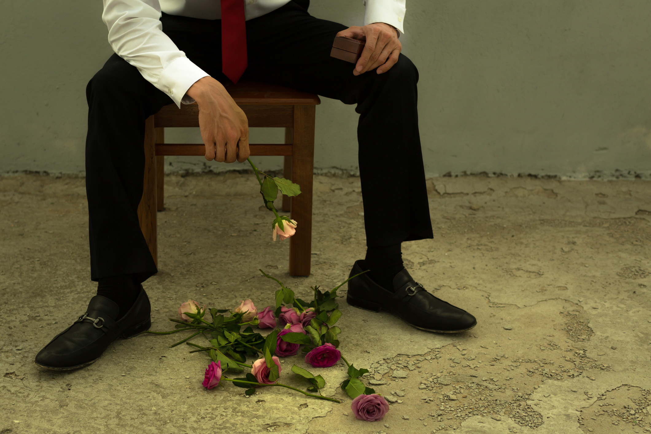 Someone heartbroken sits down, with roses from a bouquet on the floor