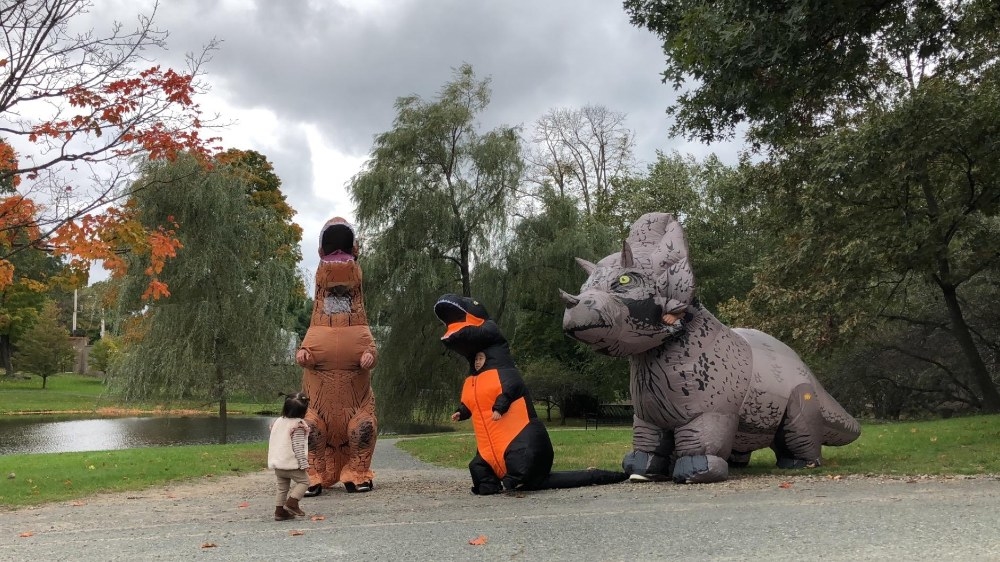 Reviewer&#x27;s photo of a person wearing the triceratops costume, along with two other people wearing other dinosaur costumes