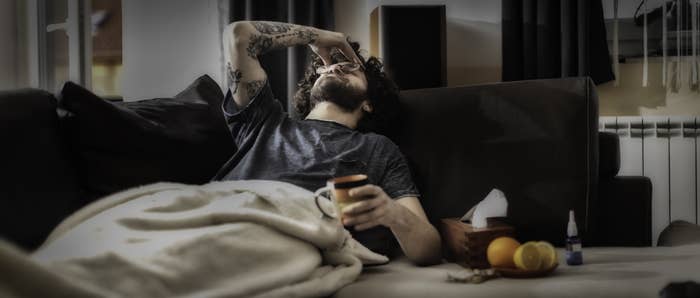 A man lies on a couch, his hand over his eyes.