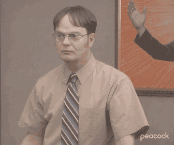 Dwight Schrute stands in a room before looking directly into the camera