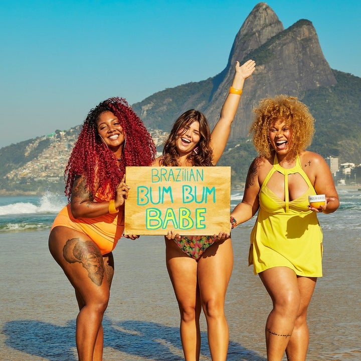 Models on a beach holding a sign that says "Brazilian Bum Bum Babe"