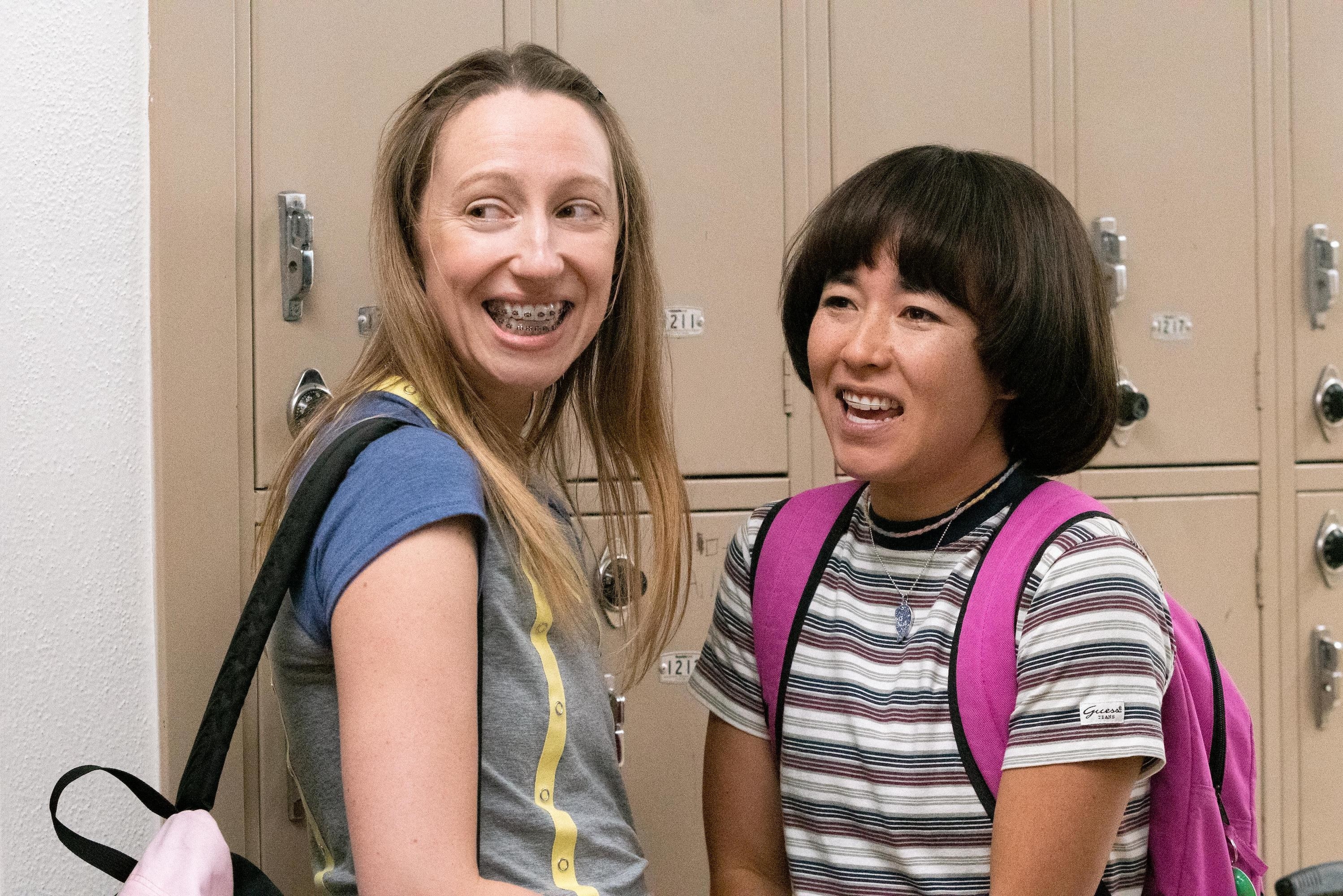 Anna and Maya show off their braces as they stand by locker with their backpacks