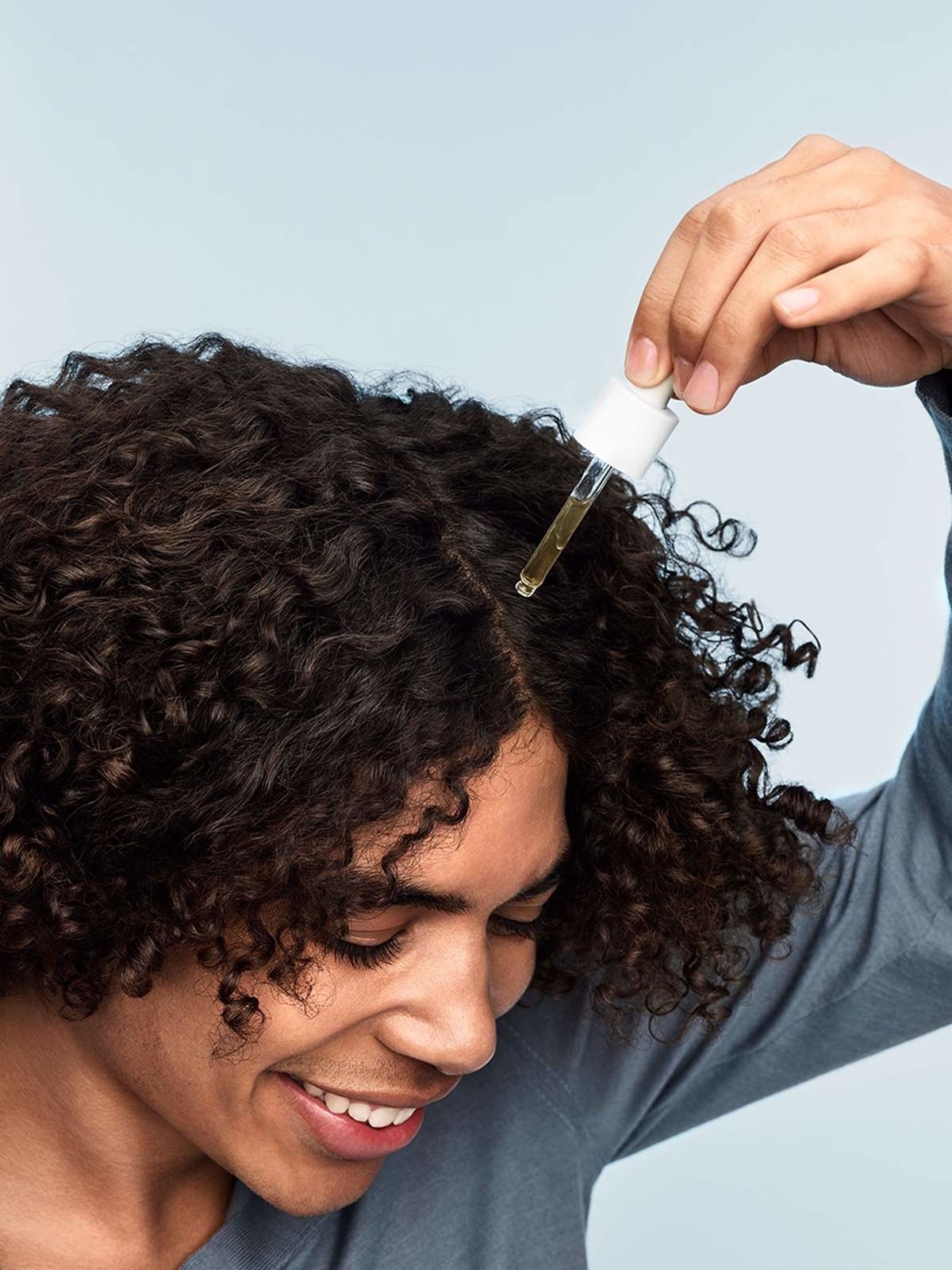 model applies a drop of the scalp treatment to their scalp