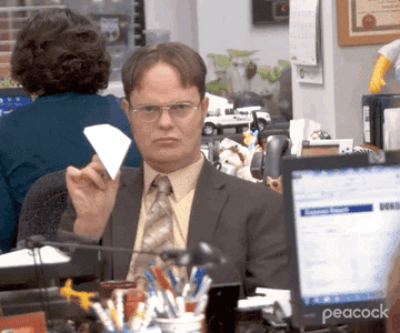 A close up of Dwight Schrute as he throws a paper airplane across the office