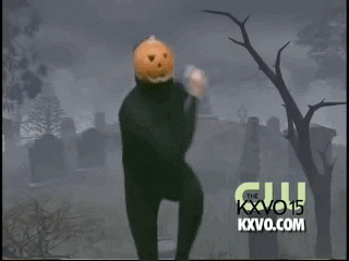 A person with a pumpkin on their head dancing in front of a cemetery backdrop
