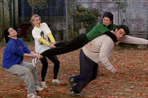 Monica and Phoebe hold Rachel's legs as she jumps on top of Joey
