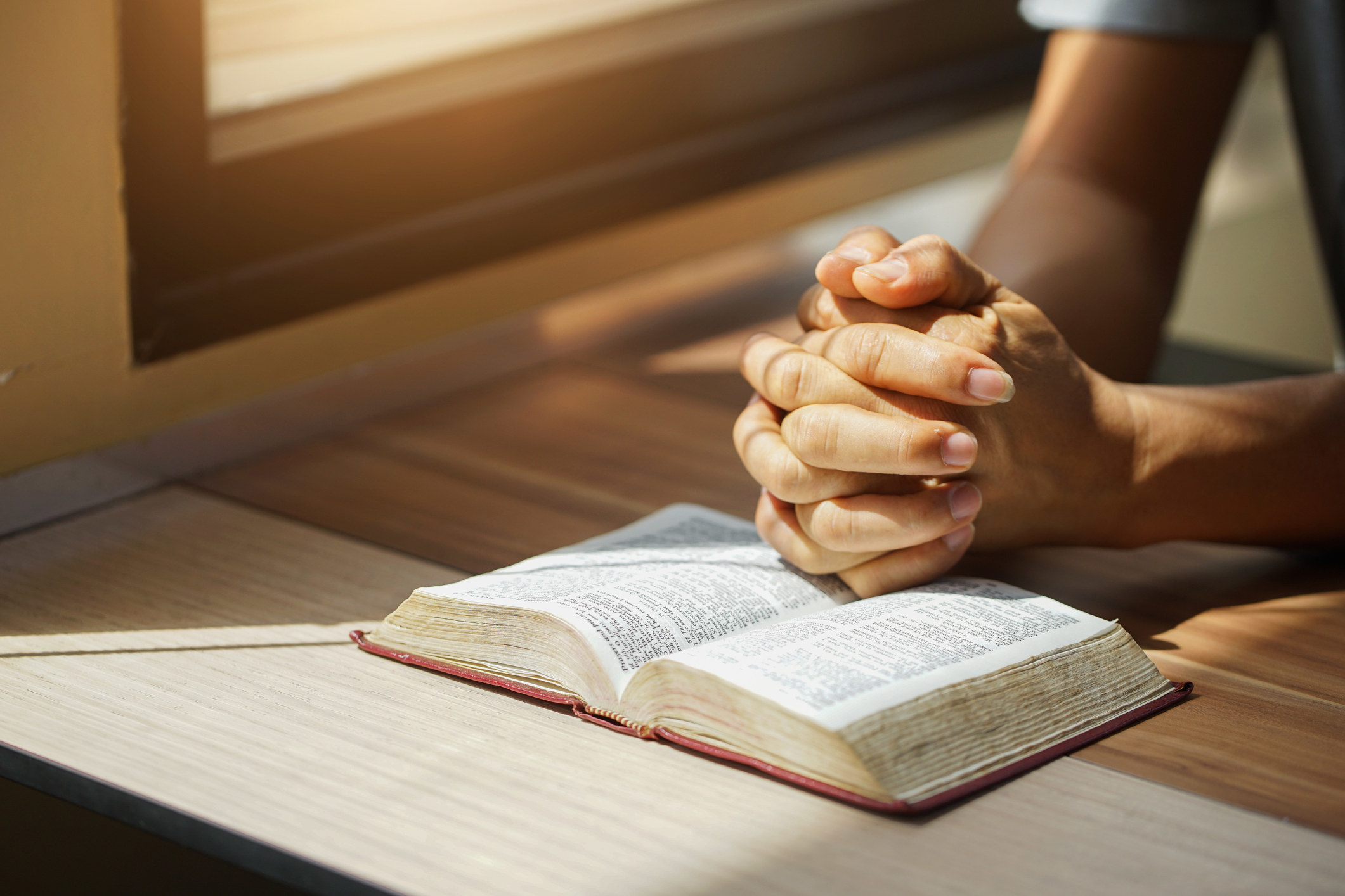 A person reading the Holy Bible and clasping their hands together