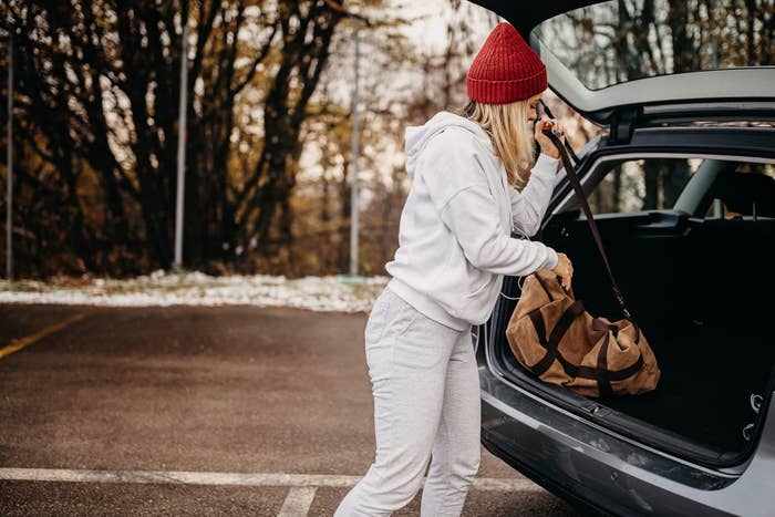 A woman takes a duffle bag from the trunk of her car.