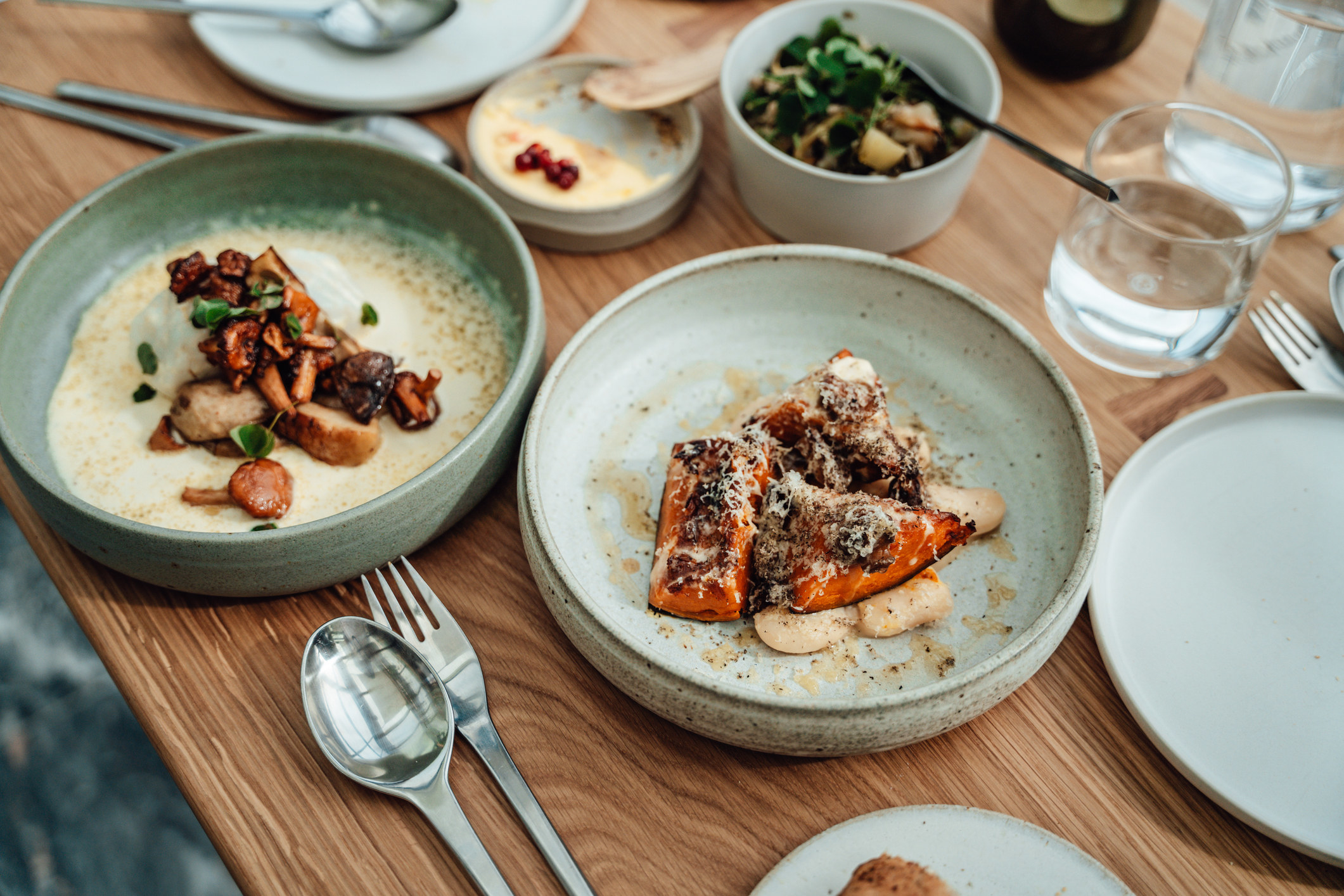 Several bowls of food, a glass of water, and utensils on a table