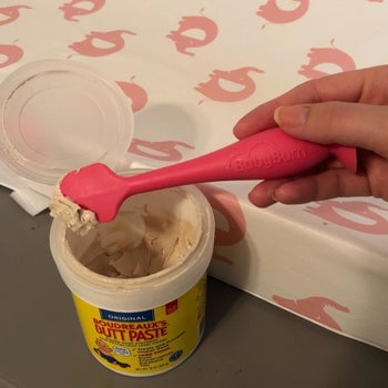Reviewer's holding the pink applicator over a jar of cream