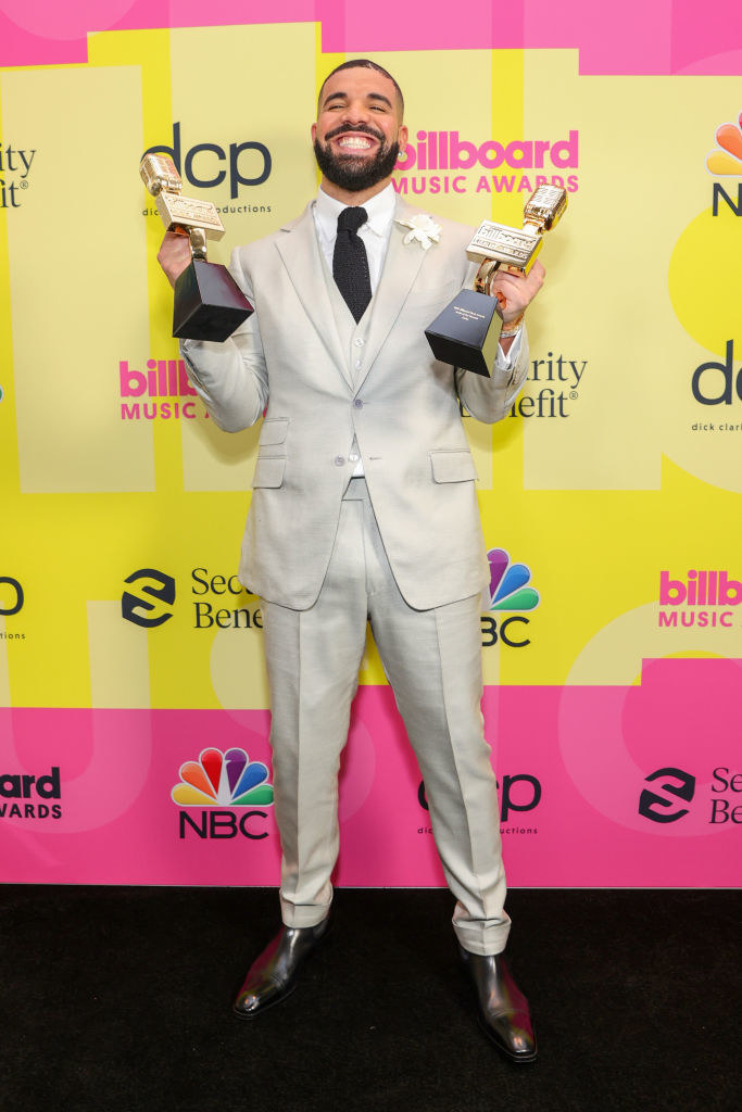 Drake on a red carpet holding two awards