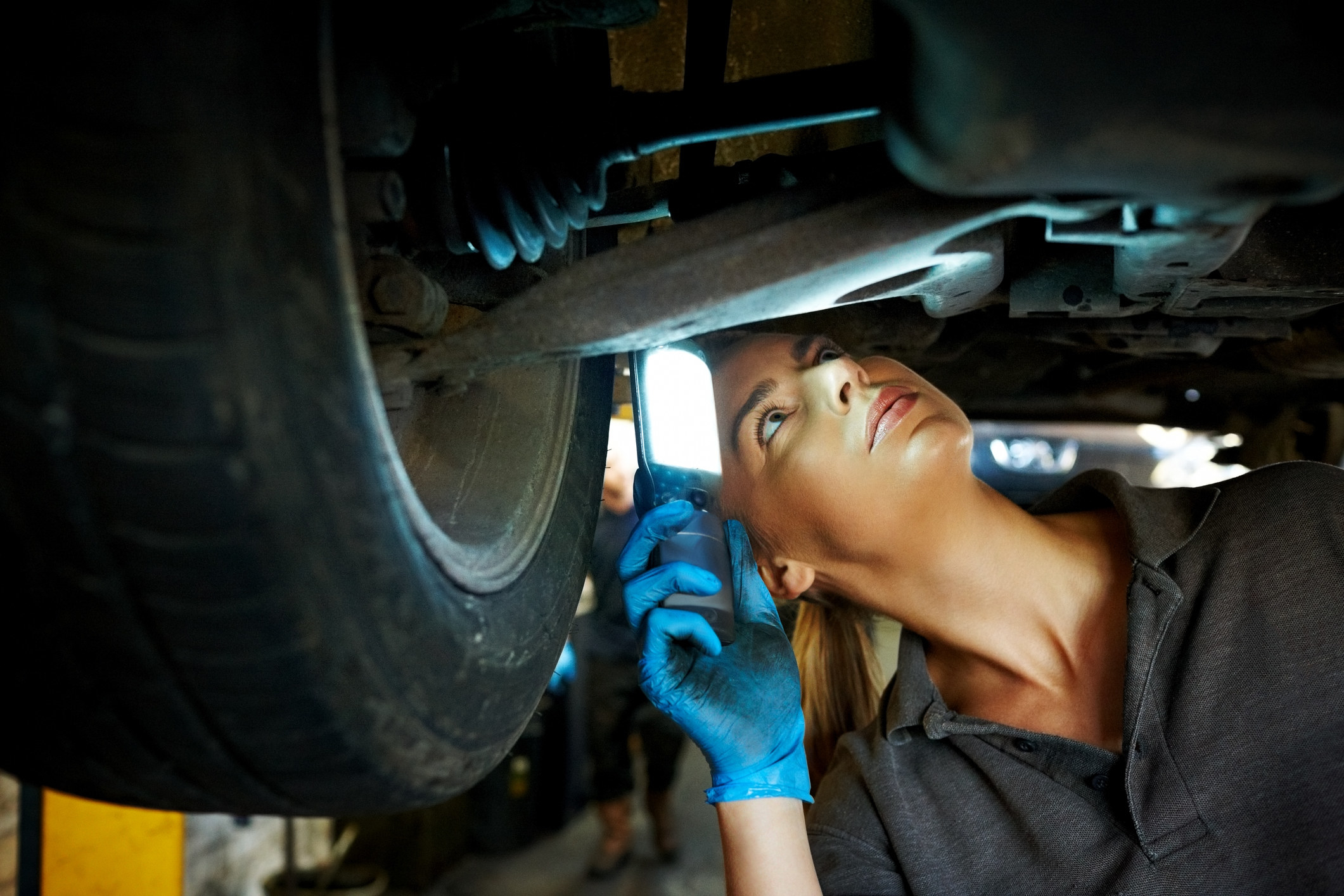 A mechanic inspects the underside of a car with a light.