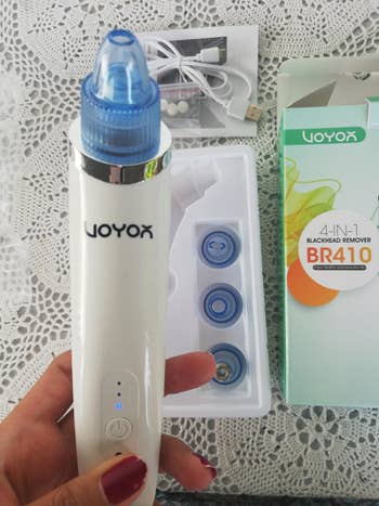 hand holds white pore vacuum in front of box with different interchangeable plastic heads