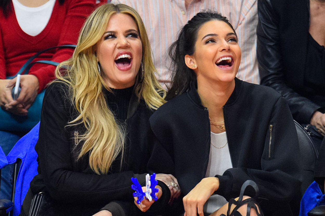 Khloe Kardashian and Kylie Jenner laughing on the sidelines of a basketball game