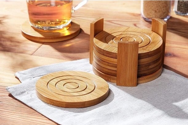 Four coasters shown in the bamboo holder with one coaster with a drink on it and another on a napkin