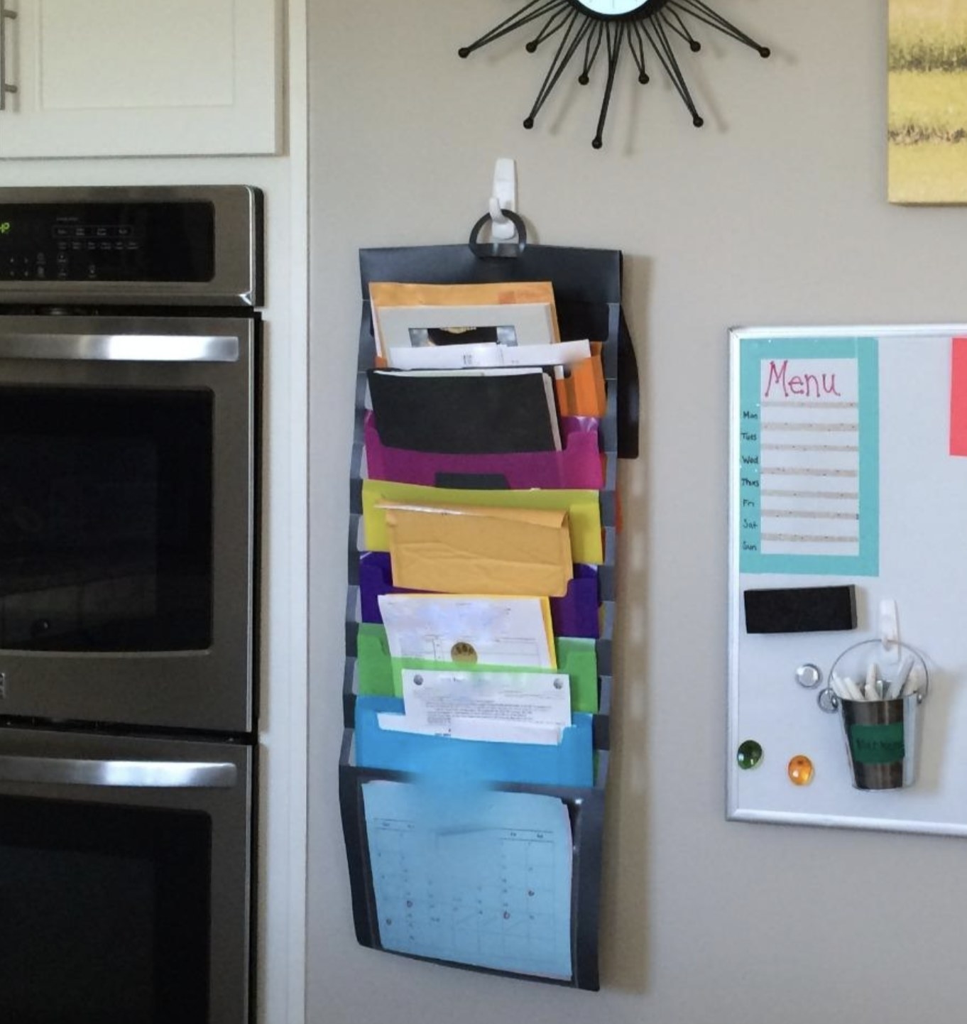 reviewer photo showing the cascading organizer on the wall in their kitchen next to a white board