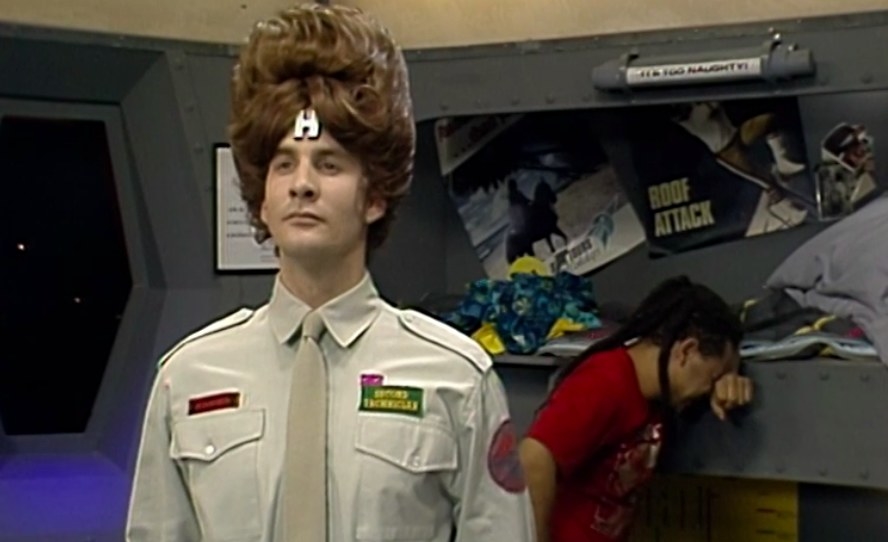Rimmer wears a beehive wig while Lister laughs behind him