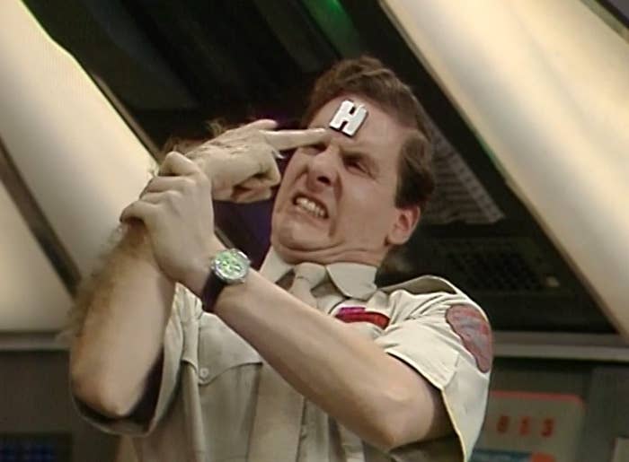 Rimmer holds his right arm back with his left arm as it attempts to poke him in the eyes — the right arm is much hairier than the left