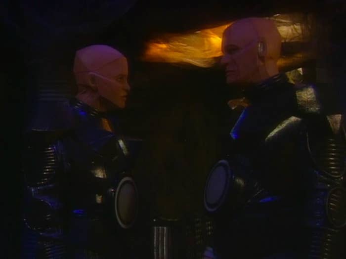 Kryten stands opposite Camille, a "female" android that looks like him