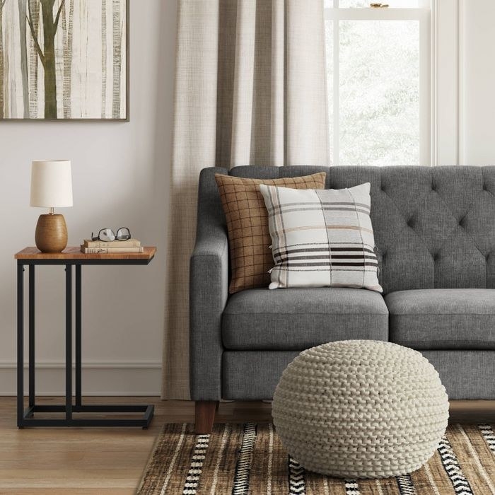 the cream pouf knit ottoman on a brown patterned rug in front of a gray couch