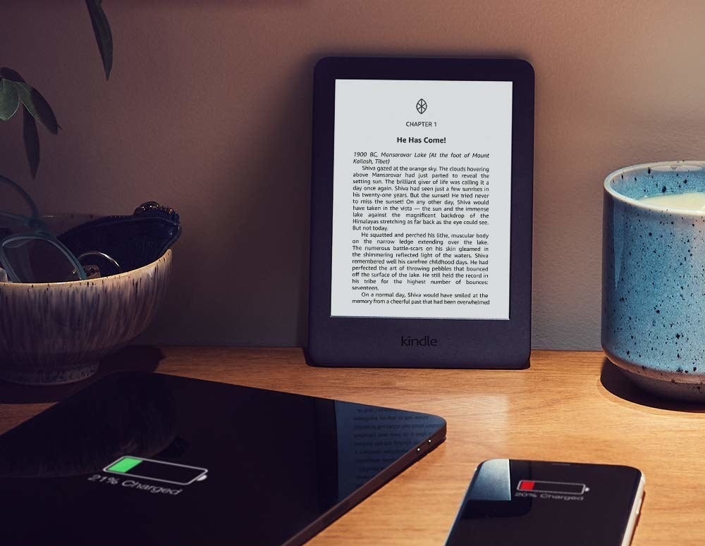 An Amazon Kindle propped up on a table alongside other devices