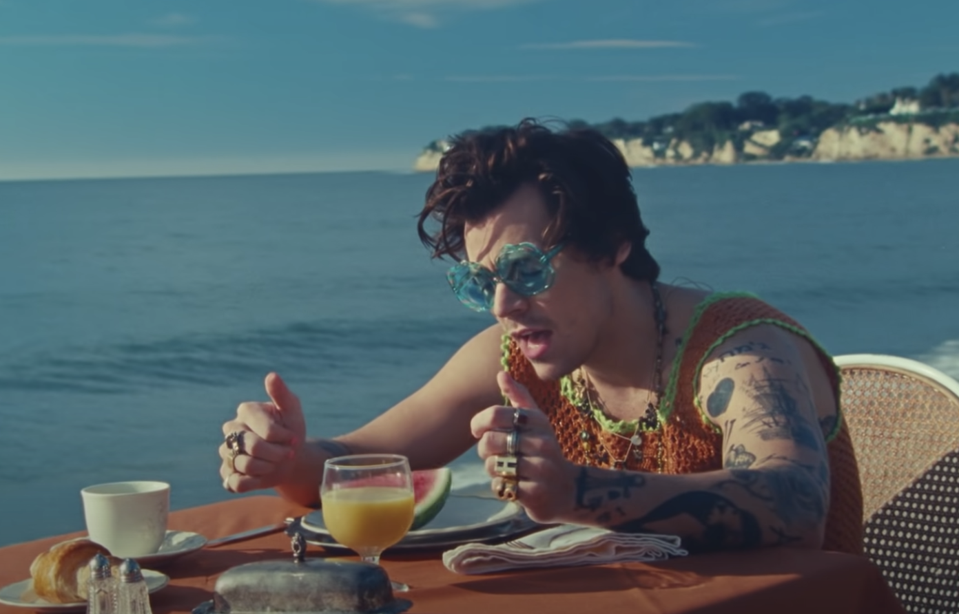 Harry sitting at a table with a plate of watermelon in front of him in a scene from the music video