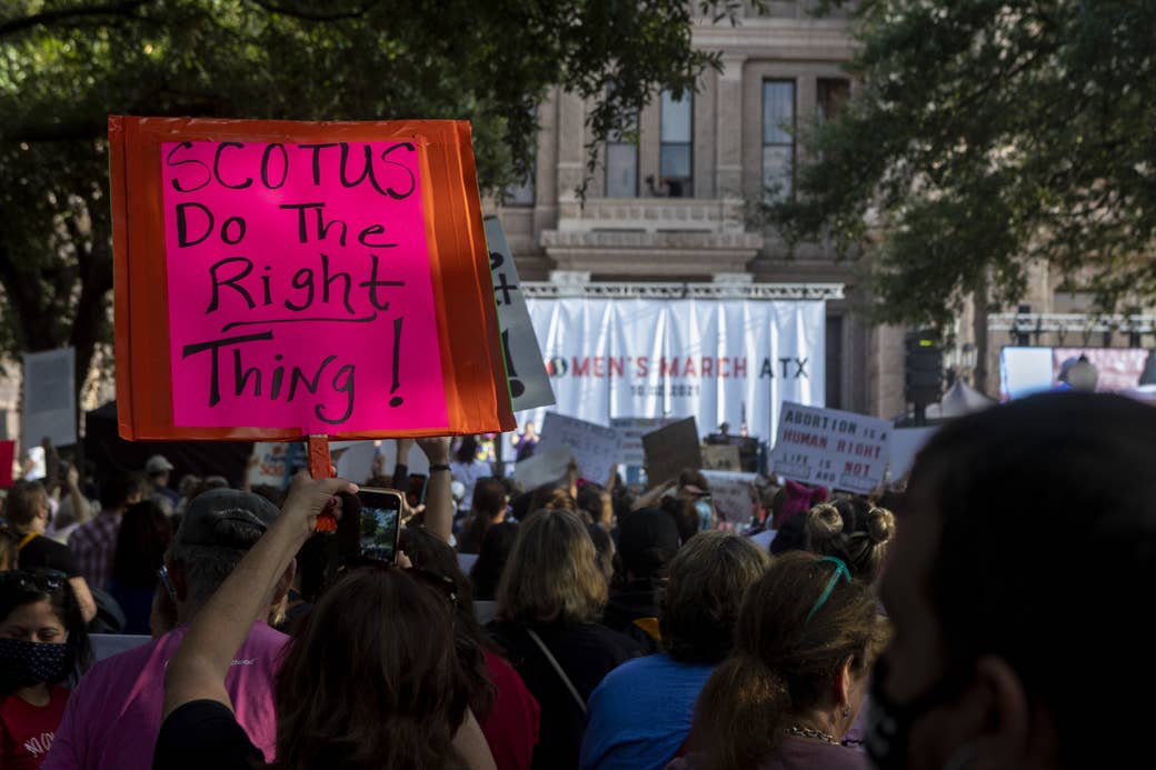 People in a crowd hold up signs, including "SCOTUS Do the Right Thing!"