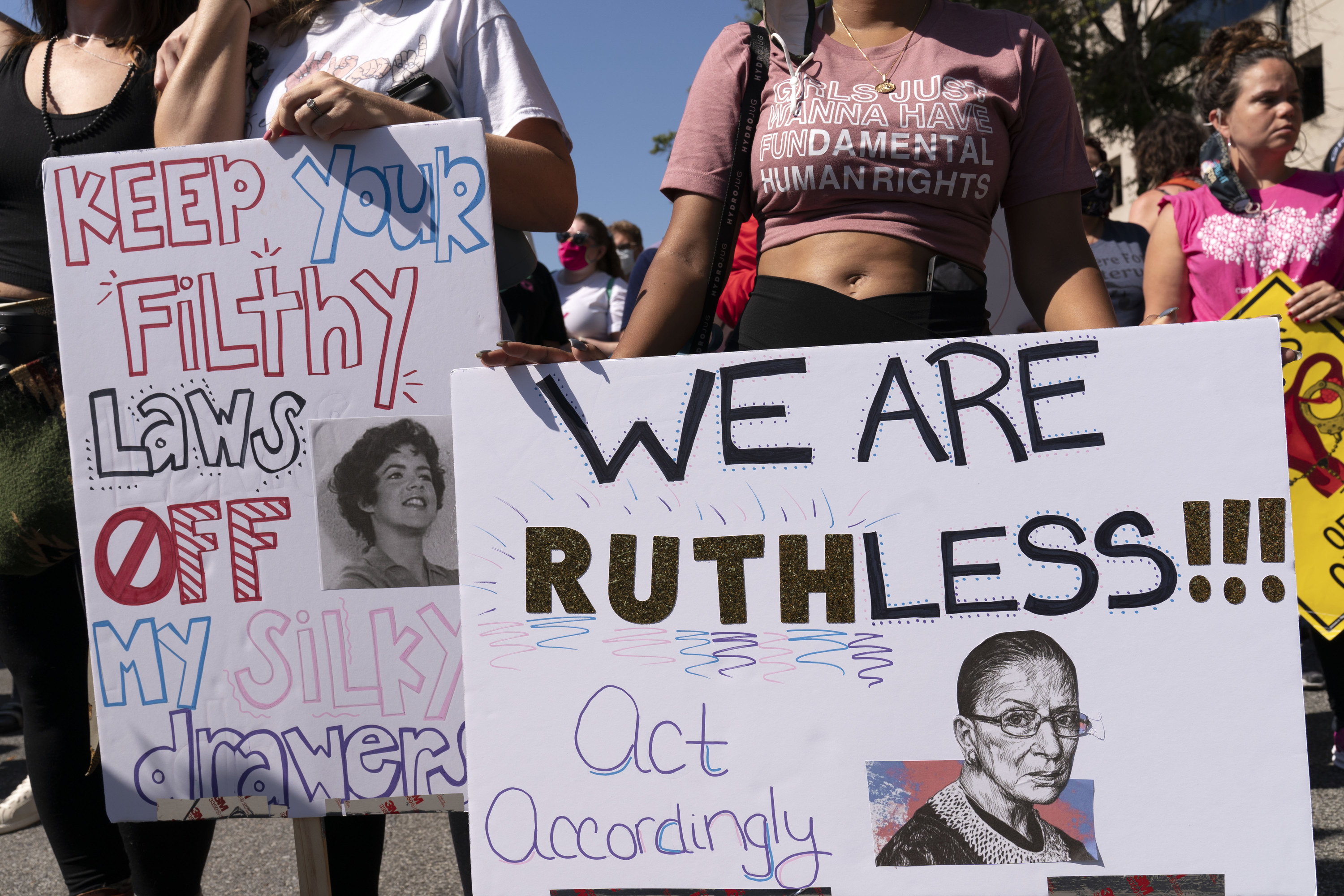 Signs held by two protesters are shown: &quot;Keep Your Filthy Laws Off My Silky Drawers,&quot; with a photo of Stockard Channing as Rizzo from &quot;Grease,&quot; and &quot;We Are RUTHless!!! Act Accordingly,&quot; with an image of the late Supreme Court Justice Ruth Bader Ginsburg