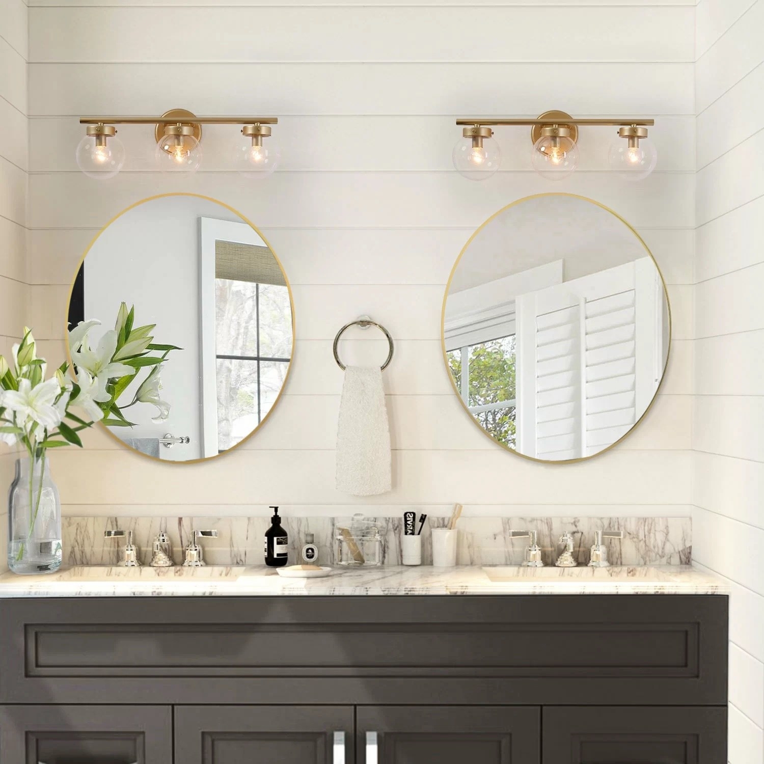 Two gold vanity lights above two mirrors and inside a bathroom.