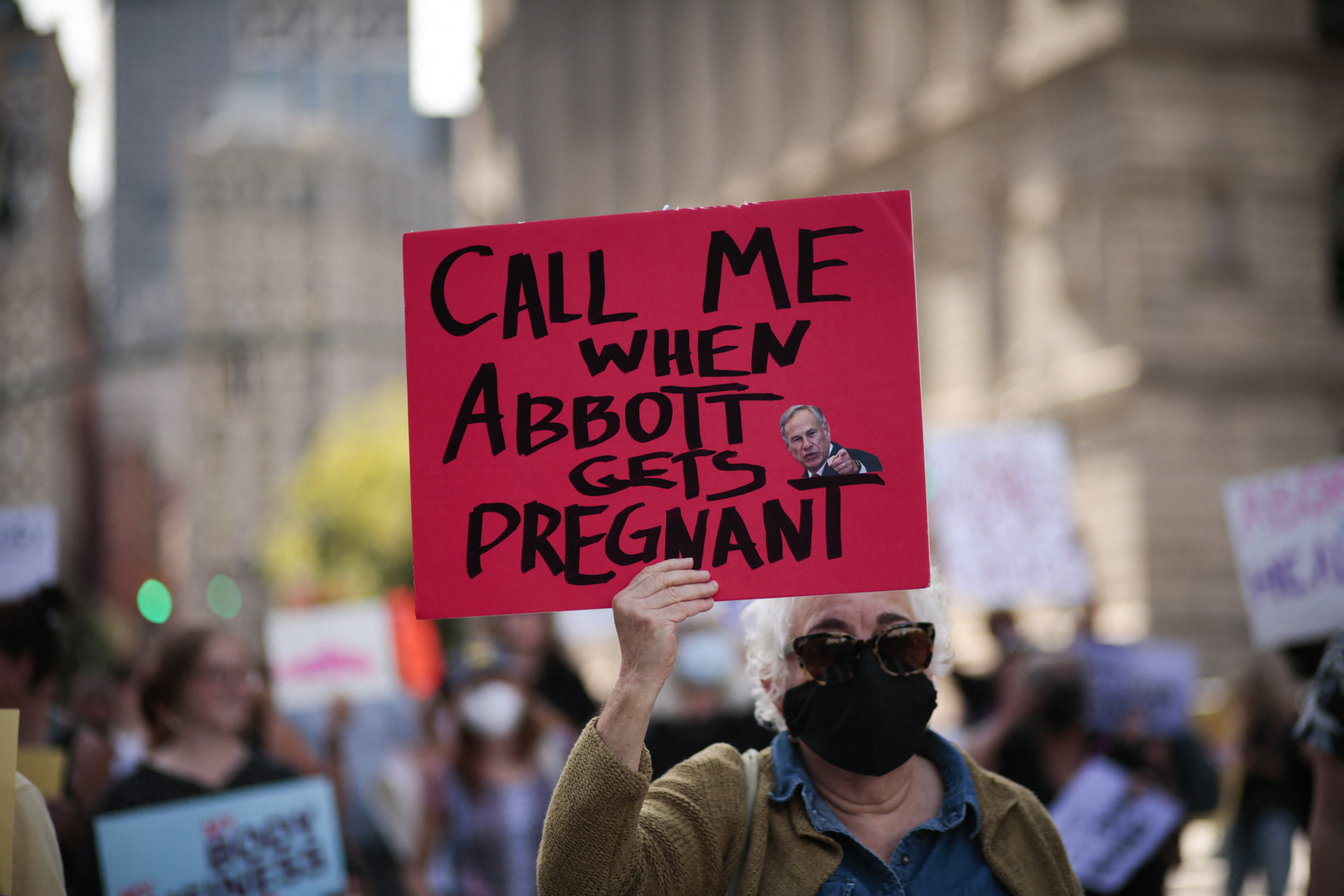 Masked person holds up a sign: &quot;Call Me When Abbott Gets Pregnant&quot;