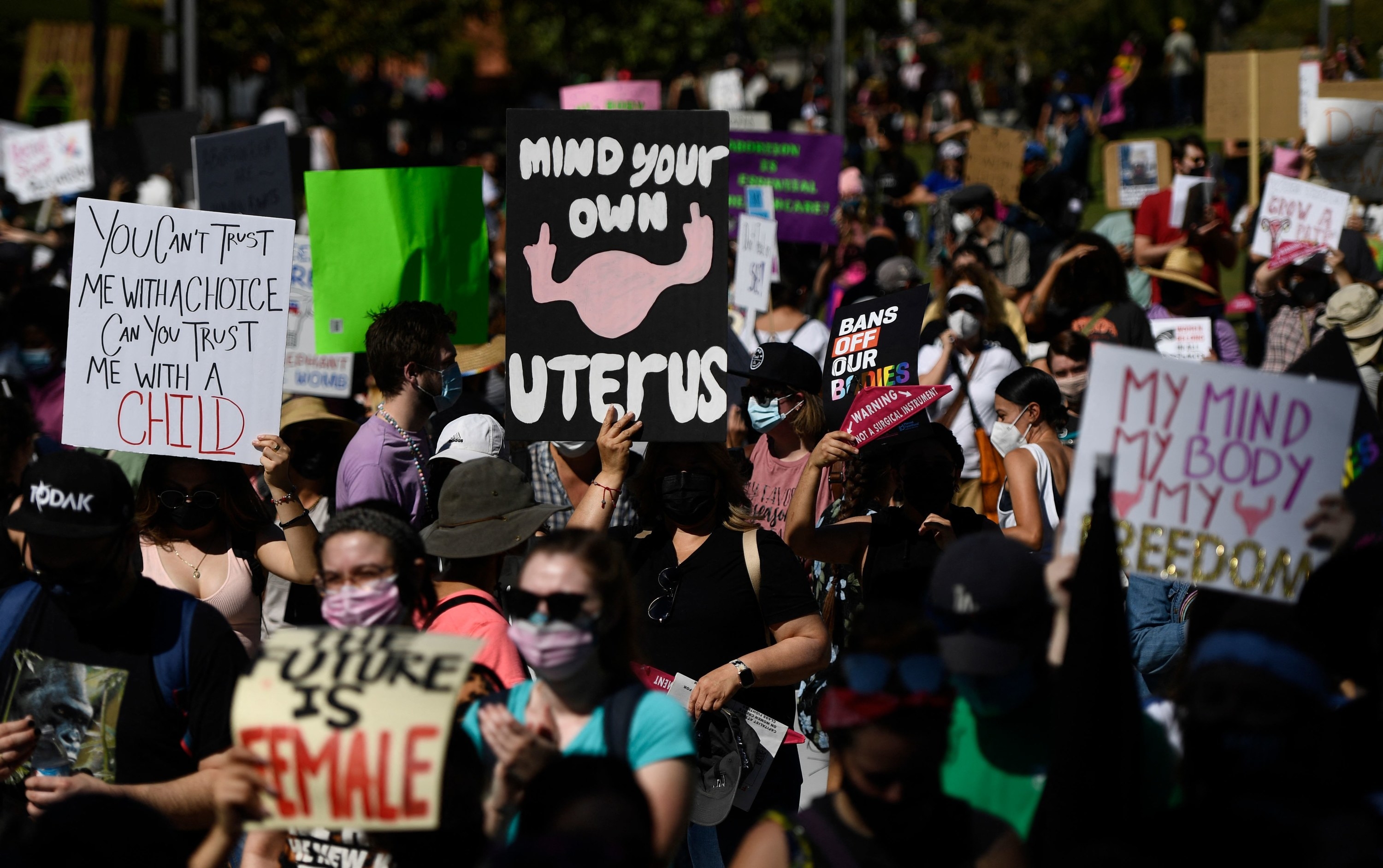 Masked protesters carry signs, including &quot;Mind Your Own Uterus&quot; and &quot;The Future Is Female&quot;