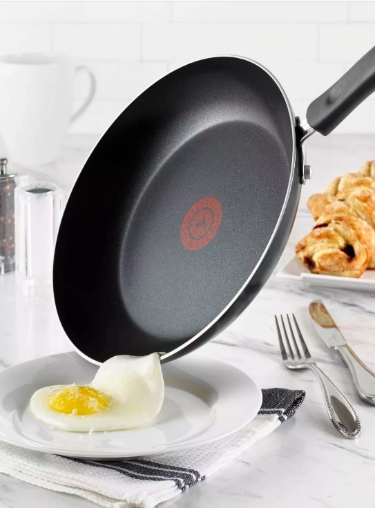 The larger fry pan sliding a egg onto a plat with no cooking residue left on pan