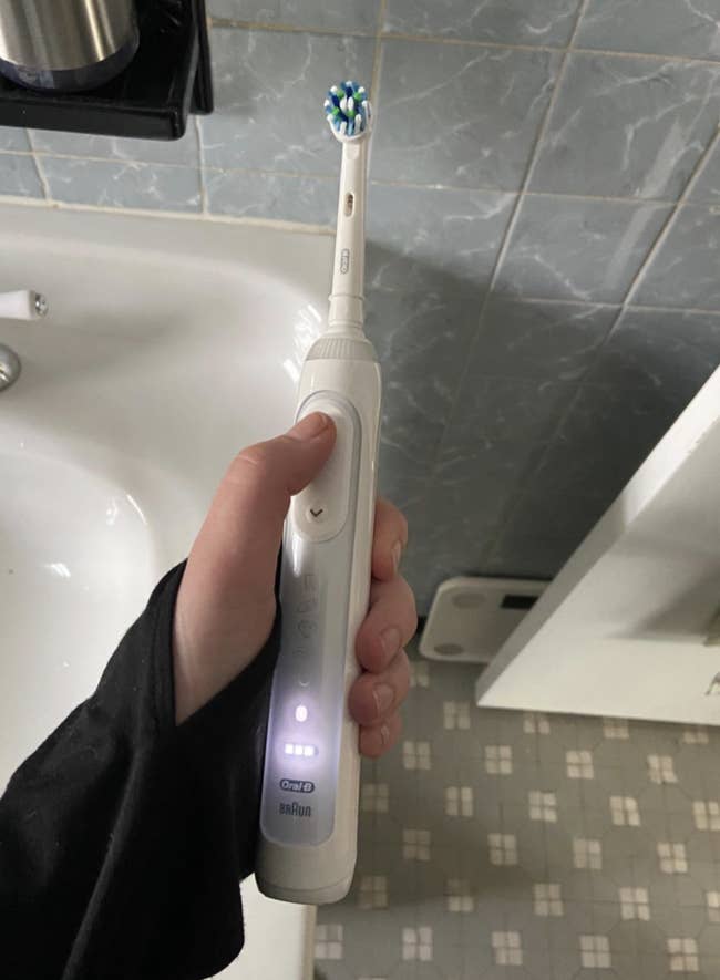 Reviewer holding a white toothbrush with settings lit up on handle